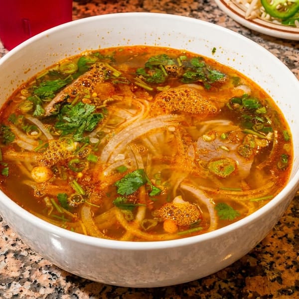 Spicy pho with noodles, beef, cilantro, and green onions in a white bowl on a granite table.
