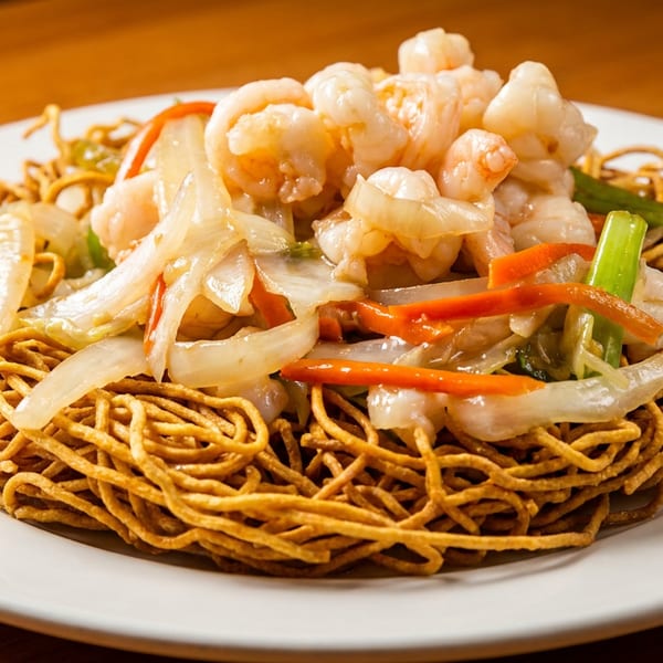 A plate of crispy noodles with shrimp, onions, carrots, and green onions.